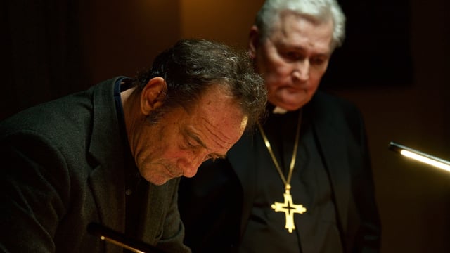 Ein Mann und ein Pfarrer mit goldenem Kreuz um den Hals. Beide in Schwarz gekleidet. Ein Mann und ein Pfarrer mit goldenem Kreuz um den Hals. Beide in Schwarz gekleidet.