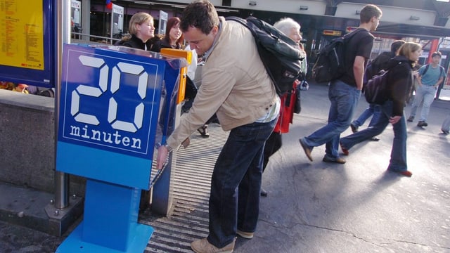 Ein junger Mann schnappt sich eine 20-Minuten-Zeitung aus der blauen Zeitungsbox. Ein junger Mann schnappt sich eine 20-Minuten-Zeitung aus der blauen Zeitungsbox.