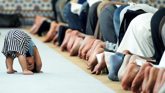Ein kleiner Junge ahmt in einer Moschee betende Männer nach.