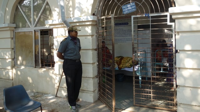 Am Eingang zur geschlossenen Frauenstation der Psychiatrie in Cuttack steht ein kräftiger Wachmann mit einem langen Holzknüppel. Am Eingang zur geschlossenen Frauenstation der Psychiatrie in Cuttack steht ein kräftiger Wachmann mit einem langen Holzknüppel.