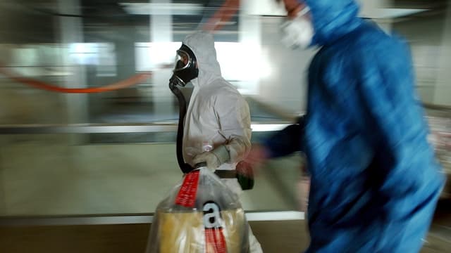 Zwei Männer in Schutzanzügen tragen Säcke mit Asbest verseuchtem Material weg Zwei Männer in Schutzanzügen tragen Säcke mit Asbest verseuchtem Material weg