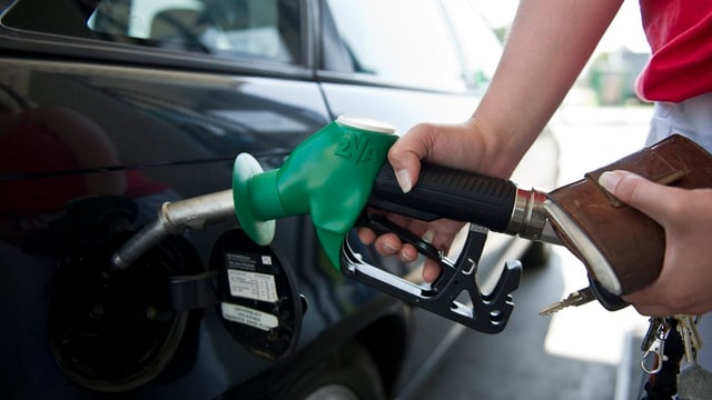 Eine Frau hält einen grün-schwarzen Tankstutzen in die Tanköffnung ihres Wagens.