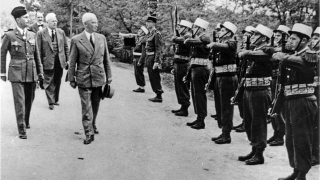 Mann in Anzug schreitet eine militärische Formation ab. Mann in Anzug schreitet eine militärische Formation ab.
