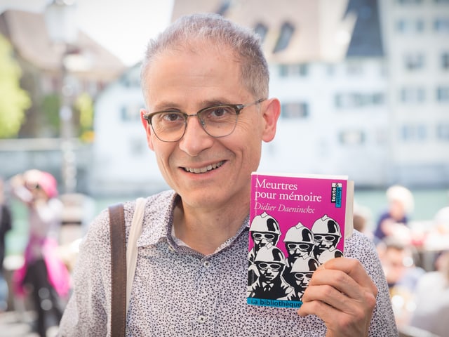 Mann mit Brille, der lächelnd ein Bild in die Kamera hält. Auf dem Buch sind mehrere gezeichnete Soldaten zu sehen.