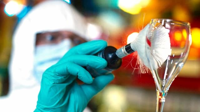 Ein Mann sucht mit einer Art Pinsel Fingerabdrücke auf einem Glas. Ein Mann sucht mit einer Art Pinsel Fingerabdrücke auf einem Glas.