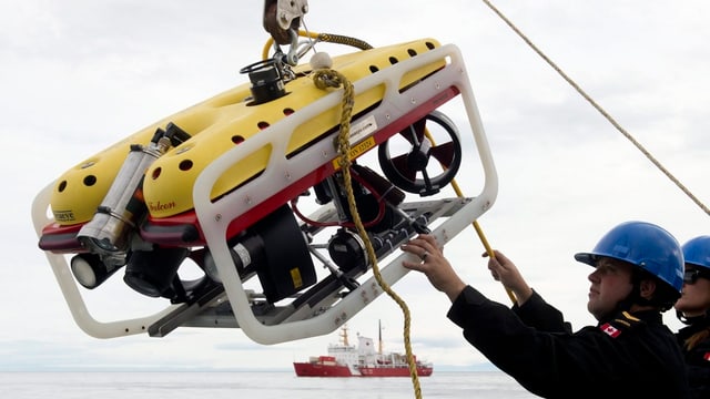Ein Mann lässt einen Unterwasserroboter über eine Seilwinde ins Wasser Ein Mann lässt einen Unterwasserroboter über eine Seilwinde ins Wasser
