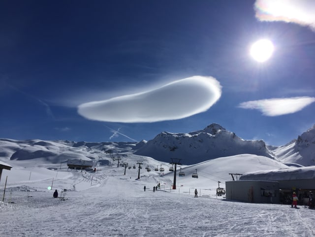 Skipiste, darüber blauer Himmel und eine bohnenförmige Wolke.