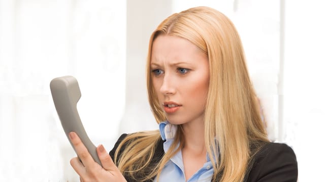 Eine Frau schaut verärgert den Telefonhörer in ihrer Hand an. Eine Frau schaut verärgert den Telefonhörer in ihrer Hand an.
