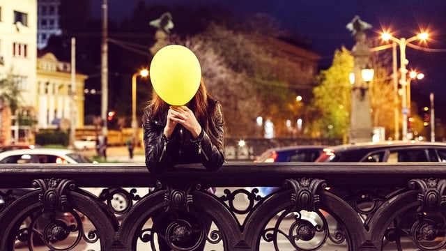 Eine Frau steht auf einer Brücke und hält einen gelben Ballon vor dem Gesicht. Eine Frau steht auf einer Brücke und hält einen gelben Ballon vor dem Gesicht.