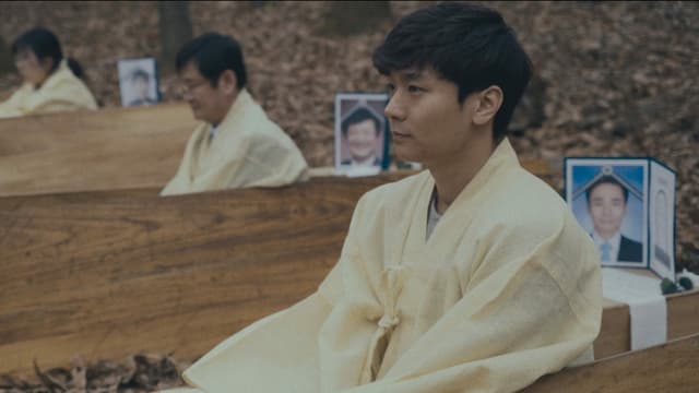 Menschen asiatischer Abstammung sitzen in Holzbänken hintereinander und haben Bild von Angehörigen hinter sich stehen. Menschen asiatischer Abstammung sitzen in Holzbänken hintereinander und haben Bild von Angehörigen hinter sich stehen.