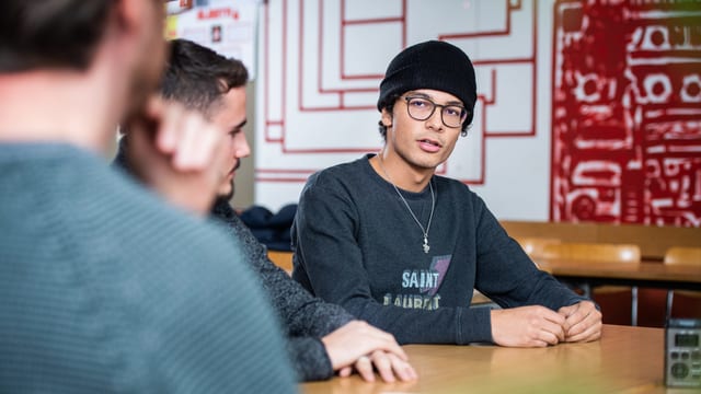 Drei junge Männer nebeneinander an einem Tisch, in ein Gespräch vertieft Drei junge Männer nebeneinander an einem Tisch, in ein Gespräch vertieft