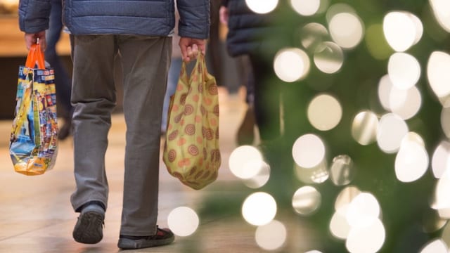 Mann hält Einkaufstüten, Weihnachtsbaum daneben. Mann hält Einkaufstüten, Weihnachtsbaum daneben.