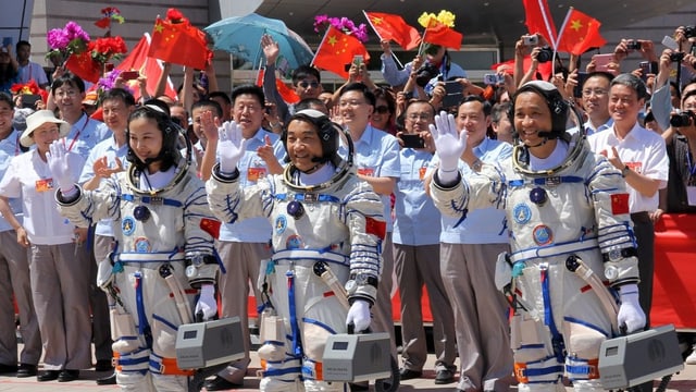 Drei Astronauten stehen winkend vor einer Menschenmenge. Drei Astronauten stehen winkend vor einer Menschenmenge.