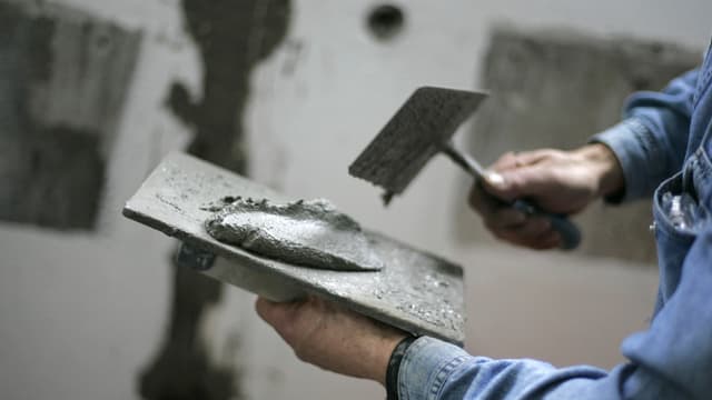 Ein Maurer hat eine Maurerkelle in der Hand mit Mörtel darauf. Ein Maurer hat eine Maurerkelle in der Hand mit Mörtel darauf.
