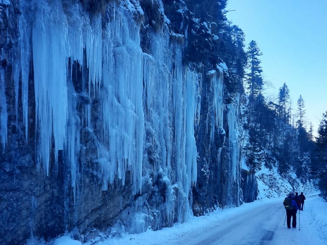 Eine Wand mit Eiszapfen und drei Männern die Wandern.