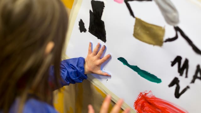 Kind drückt Hand mit Farbe auf ein Blatt Papier Kind drückt Hand mit Farbe auf ein Blatt Papier