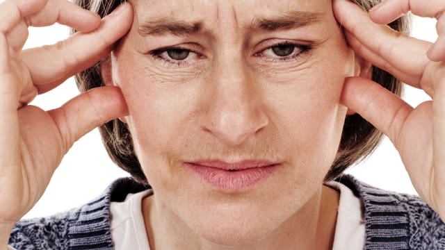 Frau mittleren Alters hält sich die Schläfen und schaut schmerzerfüllt in die Kamera. Frau mittleren Alters hält sich die Schläfen und schaut schmerzerfüllt in die Kamera.