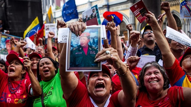 Unzählige freudige Venezolaner strecken Bilder mit Maduro und Chávez in die Kamera und schreien. Unzählige freudige Venezolaner strecken Bilder mit Maduro und Chávez in die Kamera und schreien.