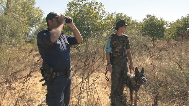 Zwei Grenzpolizisten mit Feldstecher und Hund in trockener Landschaft. Zwei Grenzpolizisten mit Feldstecher und Hund in trockener Landschaft.