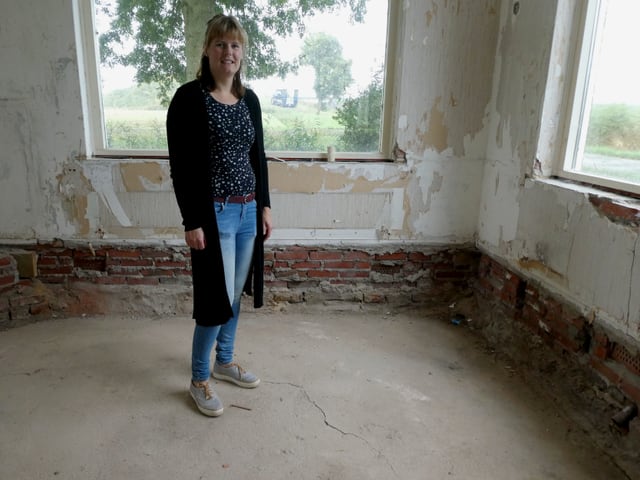 Ein Frau steht in einem Wohnzimmer, die Farbe von den Wänden abgeblättert, ein Riss im Boden. Ein Frau steht in einem Wohnzimmer, die Farbe von den Wänden abgeblättert, ein Riss im Boden.