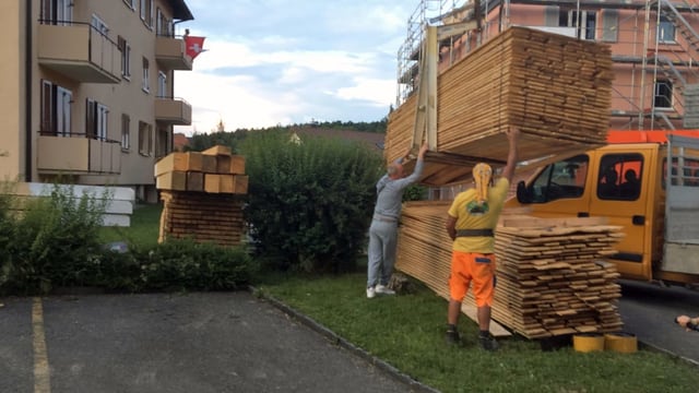 Zwei Männer laden Bretter mit einem Kran ab. Zwei Männer laden Bretter mit einem Kran ab.