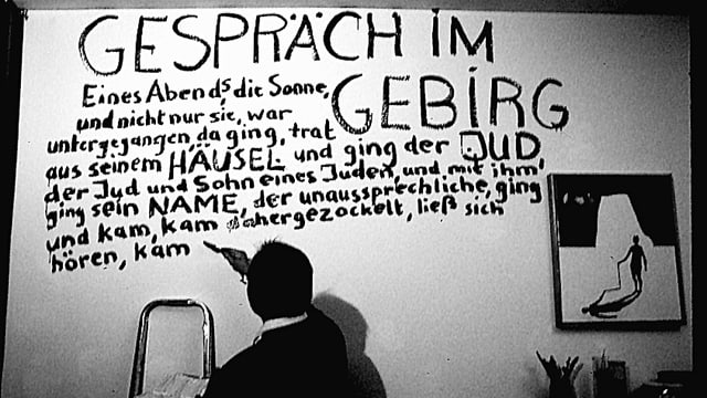 Ein Mann schreibt mit einem Pinsel einen Text an eine weisse Zimmerwand. Ein Mann schreibt mit einem Pinsel einen Text an eine weisse Zimmerwand.