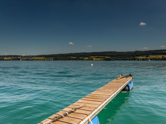 Der Steg ist frei in den erfrischenden See. Das Wasser ist türkis-, der Himmel hellblau.