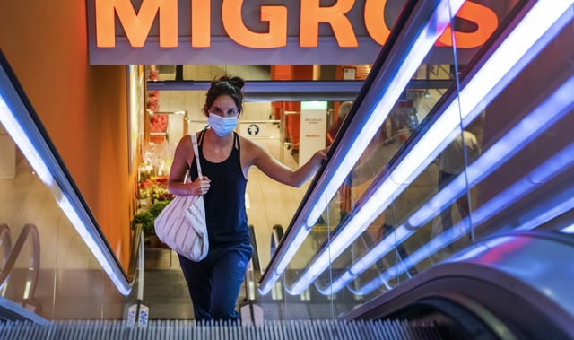 Frau auf Rolltreppe mit Maske in der Migros Frau auf Rolltreppe mit Maske in der Migros