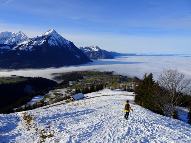 Ein Wanderer im Schnee blick hinunter auf die Hochnebeldecke. Im Hintergund hohe Bergipfel, am Himmel sind dünne Wolkenschleier vorhanden. Ein Wanderer im Schnee blick hinunter auf die Hochnebeldecke. Im Hintergund hohe Bergipfel, am Himmel sind dünne Wolkenschleier vorhanden.