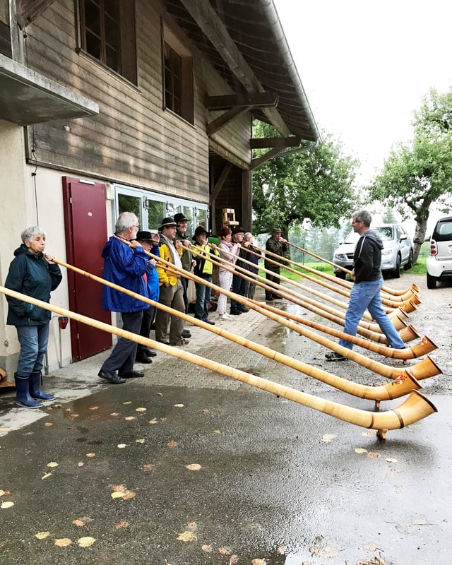 Menschen stehen unter einem Dach und halten Alphörner in den Händen. Menschen stehen unter einem Dach und halten Alphörner in den Händen.