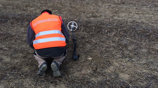 Ein Mann kniet mit einem technischen Gerät in der Wiese. Ein Mann kniet mit einem technischen Gerät in der Wiese.
