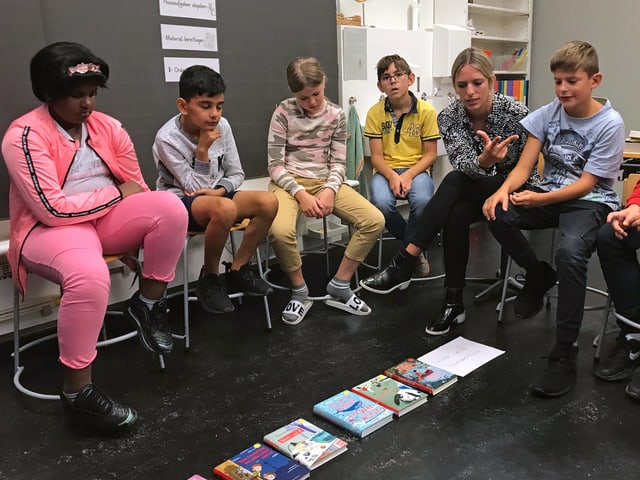 Die Kinder sitzen im Kreis um die ausgelegten Bücher und argumentieren Die Kinder sitzen im Kreis um die ausgelegten Bücher und argumentieren