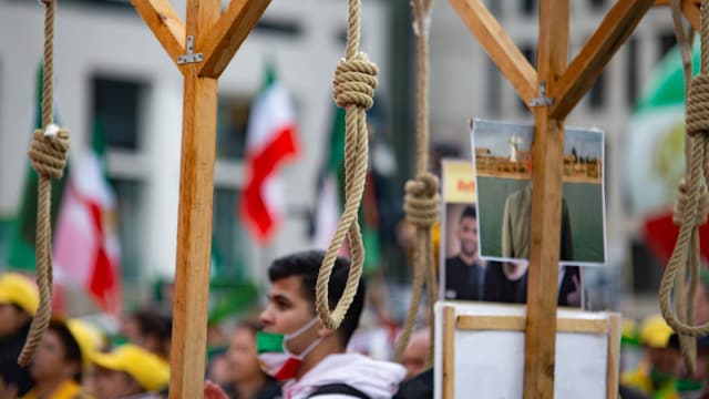 Ein Protestierender mit Irak-Mundschutz vor drei Galgen. Ein Protestierender mit Irak-Mundschutz vor drei Galgen.