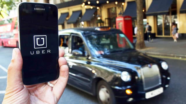 Handy mit Uber-App vor Londoner Taxi