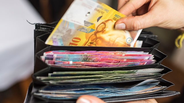 Kellnerin nimmt eine Banknote aus einem gefüllten Geldbeutel. Kellnerin nimmt eine Banknote aus einem gefüllten Geldbeutel.