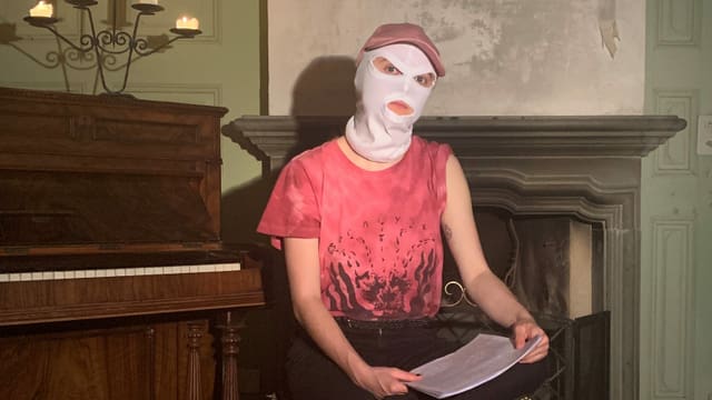 Eine Frau mit einer weissen Sturmhaube sitzt auf einem Stuhl. Auf ihrem Schoss liegt ein Stapel Papier. Eine Frau mit einer weissen Sturmhaube sitzt auf einem Stuhl. Auf ihrem Schoss liegt ein Stapel Papier.