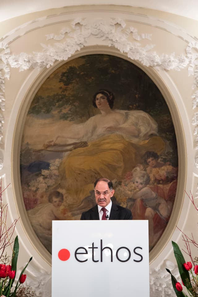 Biedermann am Redner-Pult. Im Hintergrund ein riesiges Gemälde mit einer mythologischen Frauenfigur. Biedermann am Redner-Pult. Im Hintergrund ein riesiges Gemälde mit einer mythologischen Frauenfigur.