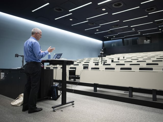 Mann hält eine Vorlesung vor Kamera in leerem Vorlesungssaal