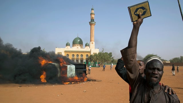 Ein Mann hält neben einem brennenden Auto vor einer Moschee in Niamey einen Koran in die Höhe. (reuters) Ein Mann hält neben einem brennenden Auto vor einer Moschee in Niamey einen Koran in die Höhe. (reuters)