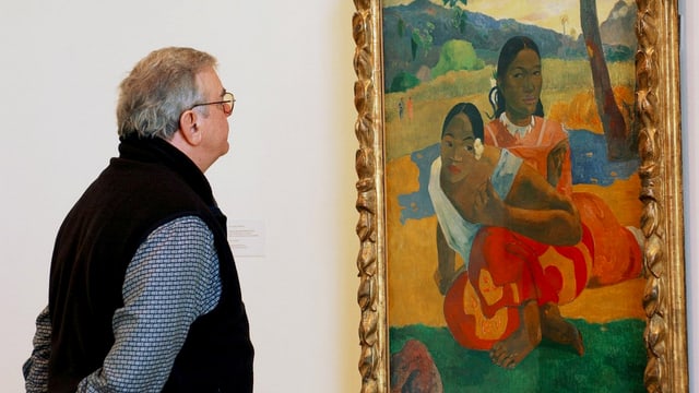 Ein Mann mit hinter dem Rücken verschränkten Armen betrachtet ein Bild von Paul Gaugin, auf dem zwei schwarzhaarige, bunt gekleidete Frauen auf dem Boden sitzen.