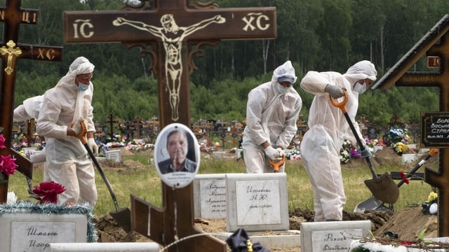 Drei Friedhofangestellte graben in Schutzanzügen Gräber für Coronaopfer. Drei Friedhofangestellte graben in Schutzanzügen Gräber für Coronaopfer.