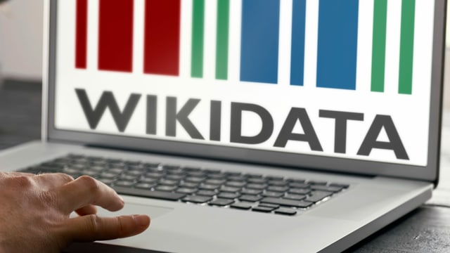 Eine Hand bedient den Laptop-Touchpad: Im Bildschirm ist das Wikidata-Logo eingeblendet. 