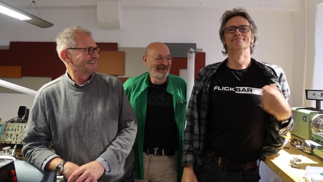 Drei Männer, einer trägt ein T-Shirt mit der Aufschrift "Flickbar" Drei Männer, einer trägt ein T-Shirt mit der Aufschrift "Flickbar"