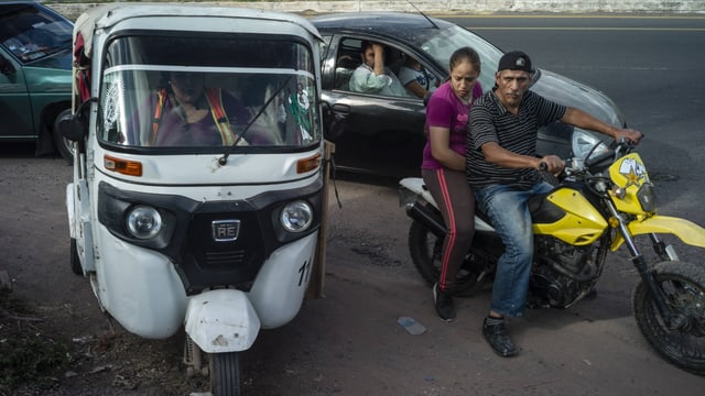 Dreirädriger Kleintransporter und zwei Personen auf einem Motorrad Dreirädriger Kleintransporter und zwei Personen auf einem Motorrad