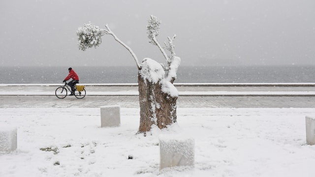 Mann auf Fahrrad auf schneebedeckter Strasse. Im HIntergrund das Meer. Mann auf Fahrrad auf schneebedeckter Strasse. Im HIntergrund das Meer.