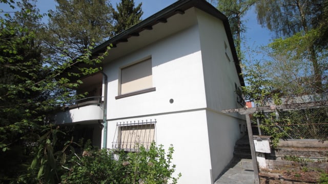 Ein älteres weisses Haus mit einem Balkon von hohen Bäumen umgeben. Ein älteres weisses Haus mit einem Balkon von hohen Bäumen umgeben.