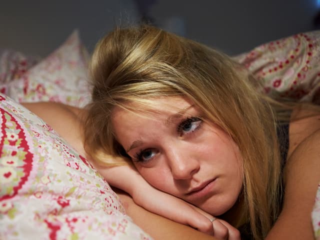 Eine junge Frau liegt im Bett und kann nicht einschlafen.