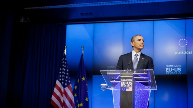 Obama an einem Rednerpult, hinter ihm EU- und US-Flagge. Obama an einem Rednerpult, hinter ihm EU- und US-Flagge.