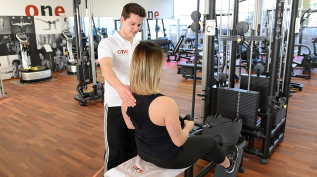Ein Fitnesstrainer trainiert mit einer Kundin an einem Gerät. Ein Fitnesstrainer trainiert mit einer Kundin an einem Gerät.