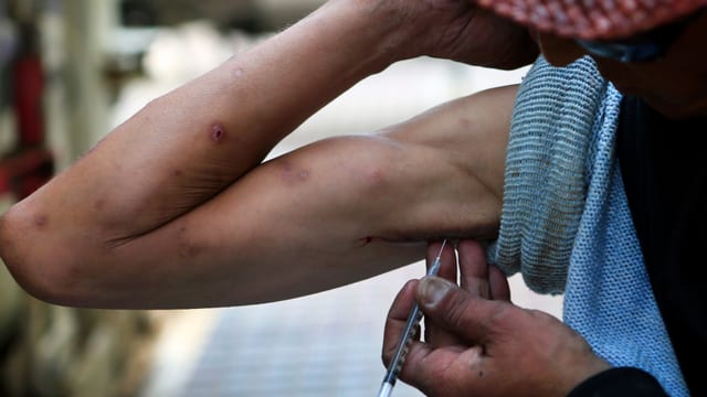 Ein Mann setzt eine Spritze an seinem Arm an Ein Mann setzt eine Spritze an seinem Arm an